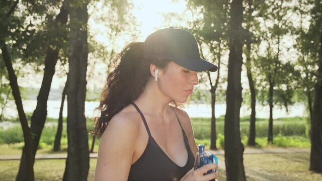 Sporty girl drinking water from a sports bottle. Fitness woman drinking water after workout outdoors close-up