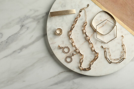 Stylish Golden Bijouterie On White Marble Table, Top View. Space For Text