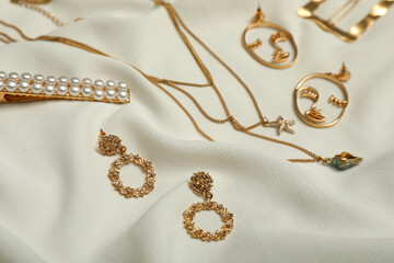 Stylish golden bijouterie on white fabric. Elegant jewelry - obrazy, fototapety, plakaty