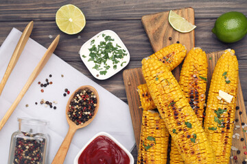 Grilled corn with sauces in bowls, spices and pieces of lime on wooden background