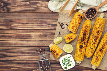 Grilled corn with pieces of lime, pepper and sauce in bowl on wooden background