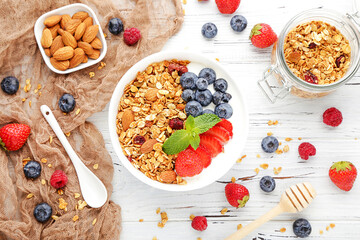 Tasty granola with fresh berries and almonds on white wooden background