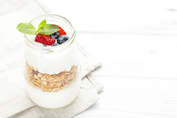 Tasty granola with cream and berries on white wooden background