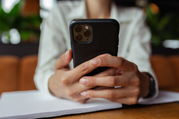 Unrecognizable crop businesswoman using mobile phone and messaging while working at table in cafe 