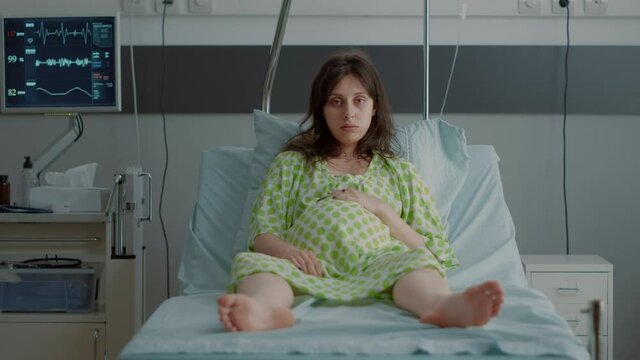 Portrait of pregnant person sitting in hospital ward bed with monitor preparing for child delivery at clinic. Caucasian young woman feeling impatient expecting labor contractions