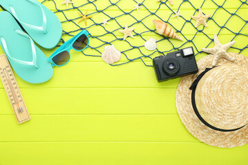 Seashells with straw hat, retro camera and flip-flops on green wooden table