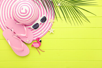 Straw hat with pair of flip-flops, sunglasses, starfishes and palm leaf on green wooden table