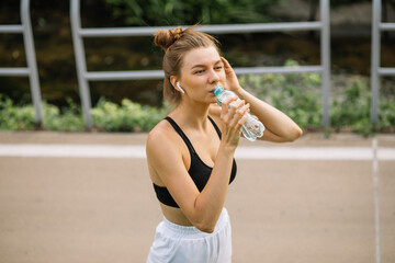 Beautiful young sportswoman woman drinks water from a plastic bottle, quenches her thirst while doing sports