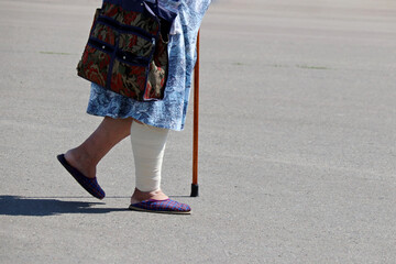Old woman with bandaged leg walking with a cane down the street. Concept of injury and wound, elderly people