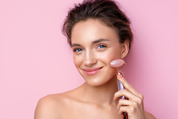 Obraz na płótnie Canvas Beautiful woman using stone facial roller. Photo of woman with perfect skin on pink background. Beauty and skin care concept