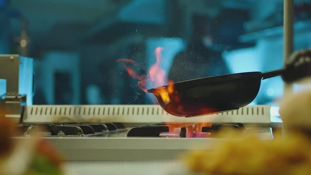 Professional chef cook flambe style . Prepares dish meat in a pan with open flames . Chef frying mixing food on gas hob in commercial kitchen . Man frying steak in flaming pan on hob in restaurant .  