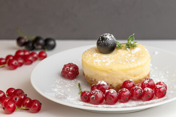 Baked homemade cheesecake with red and black currant on a white and gray background.