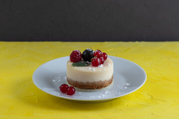 Baked homemade cheesecake with red and black currant on a white plate and yellow background.