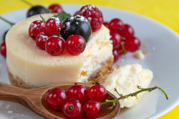 Baked homemade cheesecake with red and black currant on a white plate and yellow background, selective and soft focus.