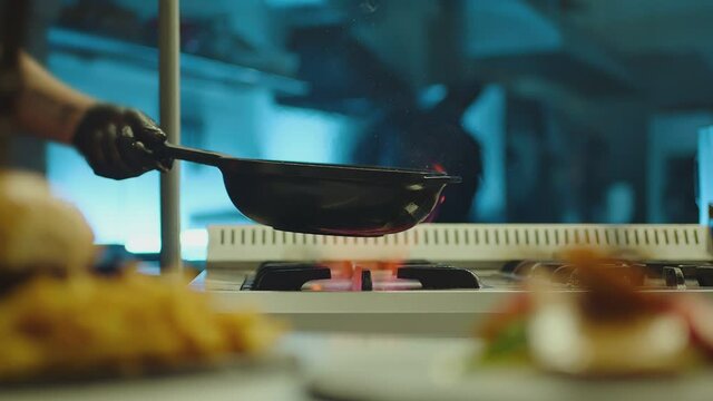 Professional chef cook flambe style . Prepares dish meat in a pan with open flames . Chef frying mixing food on gas hob in commercial kitchen . Man frying steak in flaming pan on hob in restaurant .  