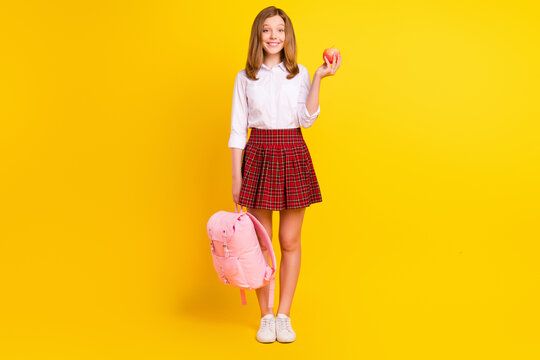 Full length photo of sweet small girl hold apple wear shirt skirt bag sneakers isolated on yellow background