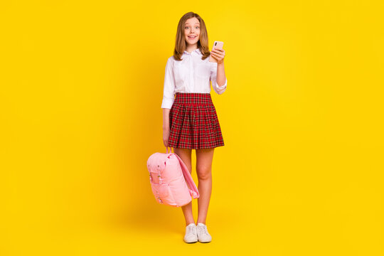 Full size photo of cute small girl hold telephone wear shirt skirt bag sneakers isolated on yellow background