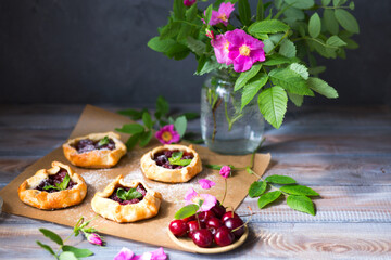 Baked small biscuits with cherries on a wooden table. Summer cakes with berries and pink flowers in the rustic style