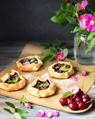Baked small biscuits with cherries on a wooden table. Summer cakes with berries and pink flowers in the rustic style