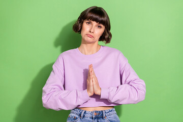 Portrait of attractive miserable brown-haired girl begging favor isolated over vibrant green color...
