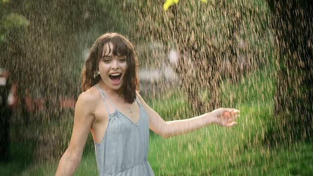 Portrait of attractive sexy young woman dancing in the rain in slow motion , rain drop on face. The girl laughs and rejoices in the summer warm rain. Concept of love, nature, happiness, freedom