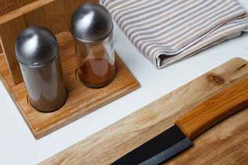 Kitchen accessories. Salt and pepper shaker, kitchen towel. Black ceramic knife, white plate. Fork and cutting board.