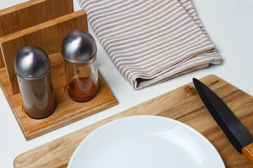 Kitchen accessories. Salt and pepper shaker, kitchen towel. Black ceramic knife, white plate. Fork and cutting board.