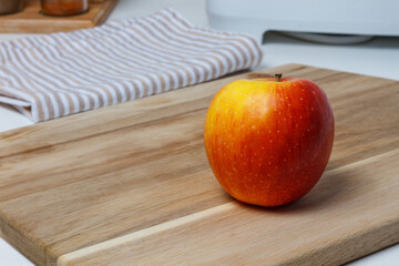 A red apple on the kitchen chopping board. A black ceramic knife and a towel.