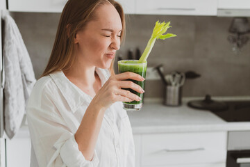 Young woman drinking healthy spinach and celery smoothie at home in the kitchen