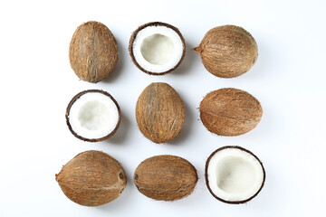 Top view shot of coconuts, whole and cracked on halves on paper textured background with a lot of copy space for text. Bacground with raw fruit of tropical palm. Flat lay.