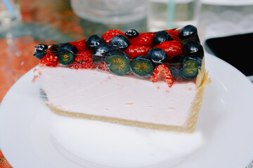 Close-up of a piece of berry cheesecake with blueberries and raspberries on a white plate. Photo for the menu of cafes, pastry shops. The concept of sweet food, pastry, recipes.