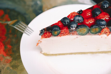 Close-up of a piece of berry cheesecake with blueberries and raspberries on a white plate. Photo for the menu of cafes, pastry shops. The concept of sweet food, pastry, recipes.