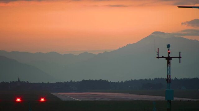 Business jet landing against dramatic and colorful sunset. Airplane descending. Long runway, Ljubljana airport, Slovenia. View of Alps in the distance. Private jet touchdown. Static shot