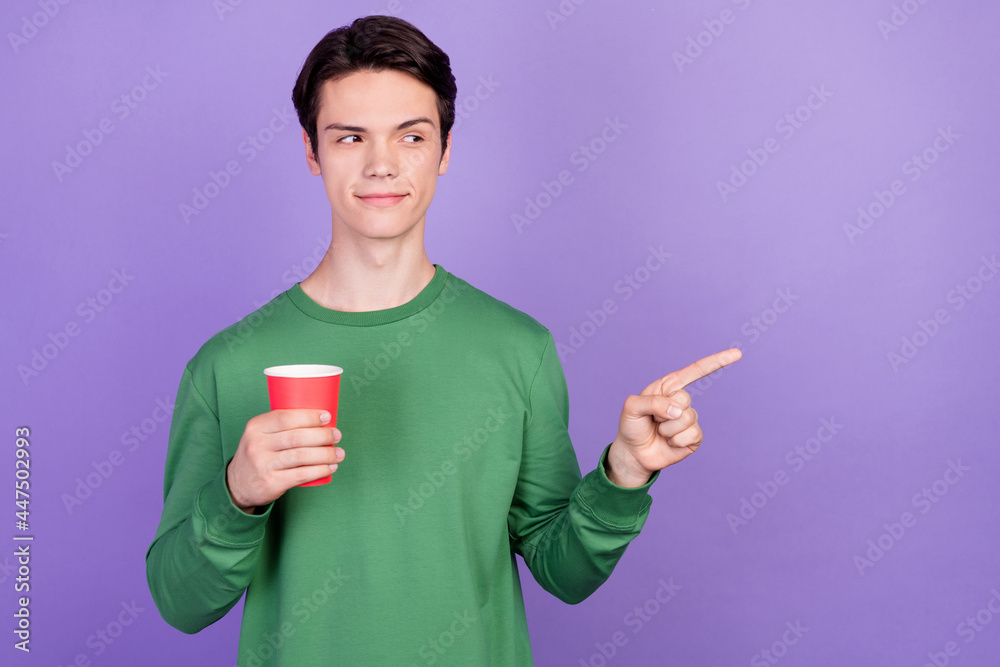 Poster photo of young guy happy positive smile hold cup point finger empty space promo choice isolated over