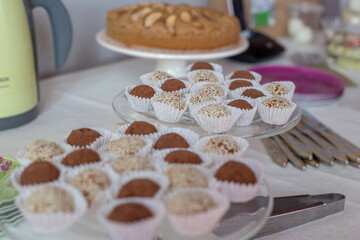 truffle candies in white and brown sprinkles in paper capsules on glass stands, apple pie in the background