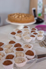 truffle candies in white and brown sprinkles in paper capsules on glass stands, apple pie in the background