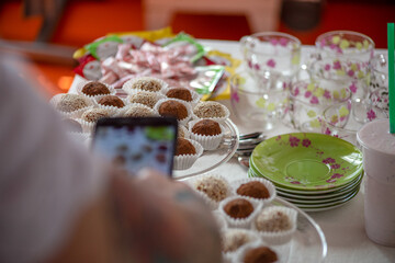 woman photographs with a smartphone candy truffles in white and brown sprinkles in paper capsules on glass coasters