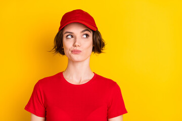 Photo of adorable thoughtful young deliver lady red workwear cap looking empty space isolated yellow color background