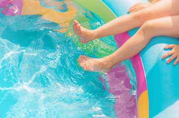 The child dipped his feet into the blue water. Bright inflatable rubber pool in the yard.