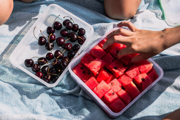 Kid's hands take fruit in a container on the beach Top view.