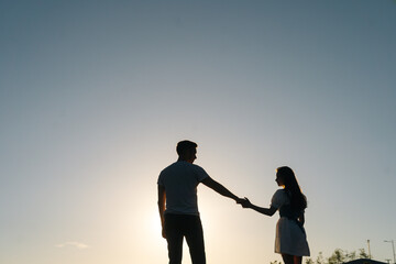 Fototapeta na wymiar Silhouette of loving young couple dancing at sunset on background of cloudless sky in evening. Happy couple in love having romantic walk outdoors enjoying time together.