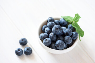 Close-up juicy and fresh blueberries with green mint leaves on white wooden table. Soft focus