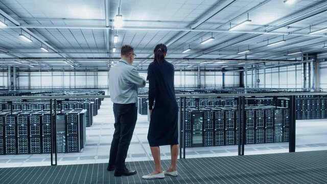 Data Center Female System Administrator and Male IT Specialist Talk, Use Laptop. Information Technology Engineers work on Cyber Security Network Protection in Cloud Computing Server Farm.