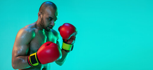 Flyer. One professional boxer in red gloves training, exercising isolated over blue green background in neon light.
