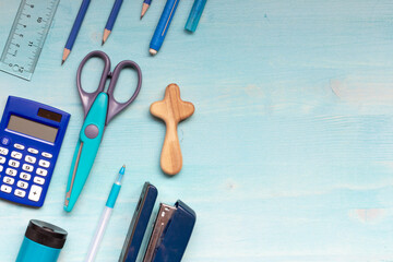 school supplies with small wooden cross on blue wood background with copy space 