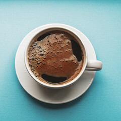 Black coffee in a white cup on blue background, top view.