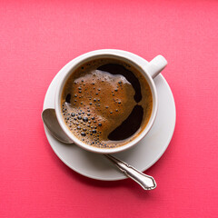 Black coffee in a white cup on blue background, top view.