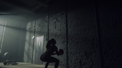 Woman doing squats with heavy weight ball. Girl throwing fit ball against wall 