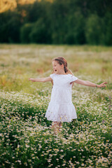 Naklejka na ściany i meble A girl in a white dress with a hat is spinning with outstretched arms in a field of daisies