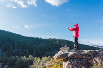 man on a rock dressed in red taking a photo of the landscape with a cell phone